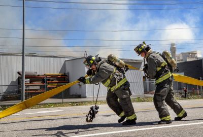 Firefighters lay down hoses along Highway 97A Friday afternoon, July 15, 2022, as smoke and fire come from Keyes Fibre’s manufacturing plant in the background. Chelan County Fire Department was hoping to contain the fire to two of seven areas inside the building. (Don Seabrook | The Wenatchee (Washington) World)